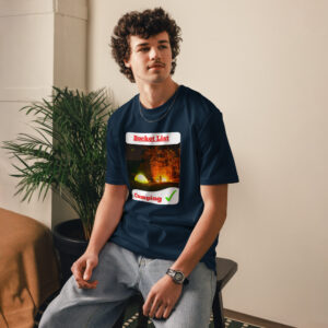 Young man seated indoors wearing a navy graphic tee with 'Bucket List' and a camping image; neutral background and green plant nearby.